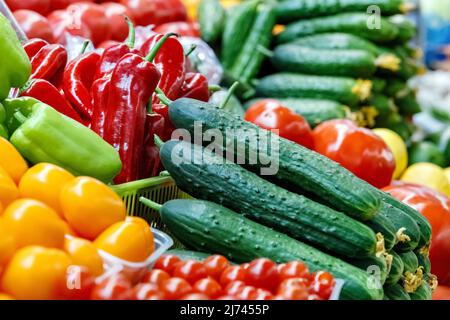 Fresh tomatoes, peppers and cucumbers on counter of grocery market. Vegetarian food trade. Stock Photo