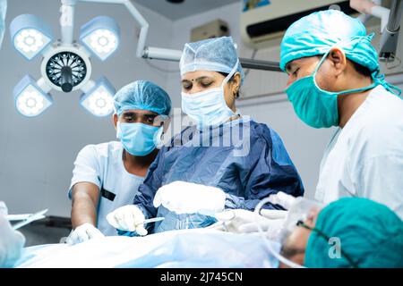 Woman surgeon with supporting practitioners busy doing surgery at operating room - concept of teamwork, healthcare treatment and woman empowerment. Stock Photo