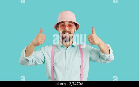 Cheerful funny charismatic young man showing thumbs up isolated on turquoise background. Stock Photo
