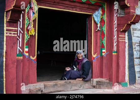 Elderly Tibetan grandma sitting at a small temple entrance Stock Photo