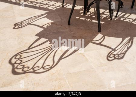 Cafe without visitors on the open terrace. Shadows from empty chairs. Stock Photo