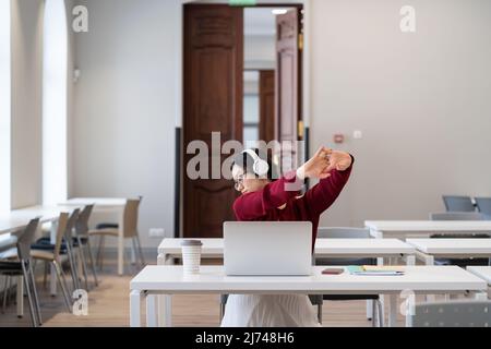 Tired asian female student sitting in library taking break during online learning on laptop Stock Photo