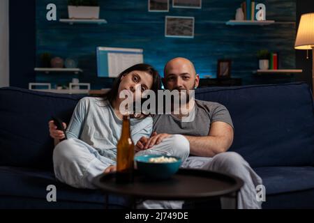 POV of young partners watching movie on TV screen, doing leisure activity and relaxing on couch. Man and woman looking at film on television channel to have fun, entertainment and excitement. Stock Photo