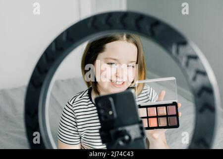 Teen girl recording video review blog using smartphone and LED lamp at home. Blogging, videoblog, makeup concept. Stock Photo