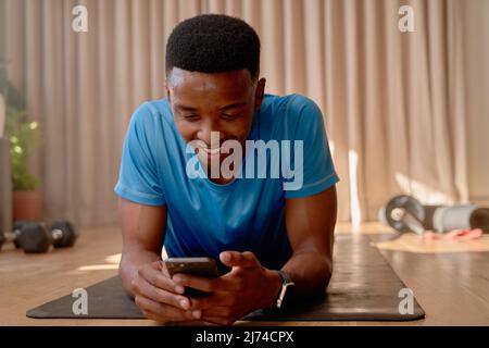 Young happy black African american male working out from home taking a break on his cellphone lying on an exercise mat Stock Photo