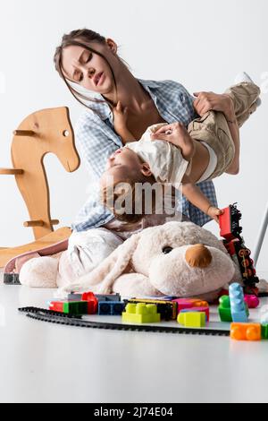 tired woman holding son while playing with him near toys on white Stock Photo