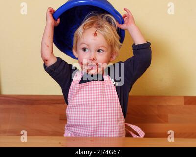 after licking the mixing bowl girl is holding the mixing bowl over her head; she has a funny choclate mouth Stock Photo