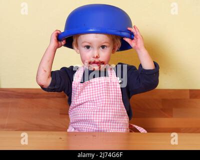 after licking the mixing bowl girl is holding the mixing bowl on her head; she has a cute choclate mouth Stock Photo