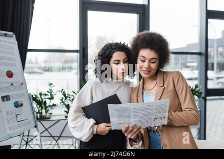 Multiethnic businesswomen reading newspaper in office Stock Photo