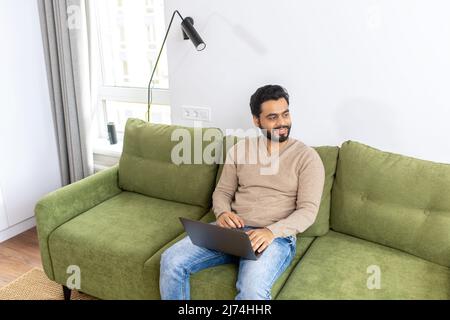 High angle view of the happy smiling business man distantly working from home. Successful male freelancer sitting at the sofa, using laptop, develop a project. Online study concept Stock Photo