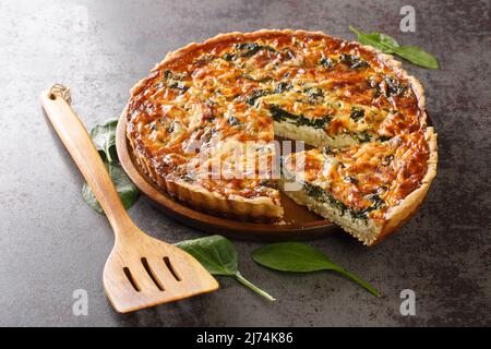 Savory tart of rich egg custard, spinach and cheese with cut out a slice on the plate on the gray table close-up. Hotizontal Stock Photo