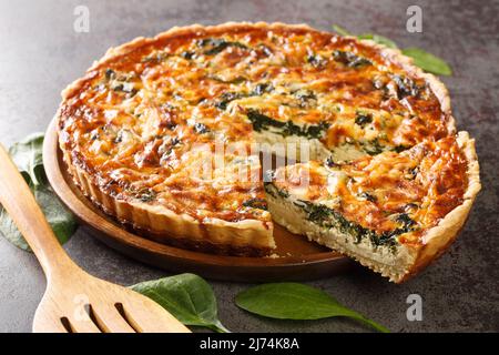 Quiche Florentine with spinach, cheese, eggs and spices on gray table with spatula, close-up. Hotizontal Stock Photo