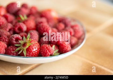 Plate of fresh strawberries and raspberries in a kitchen, laid on a beige floor tile Stock Photo