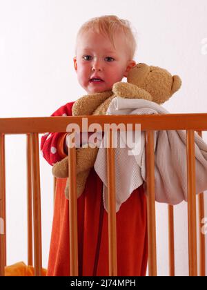 little girl stands in bed holding his teddy Stock Photo