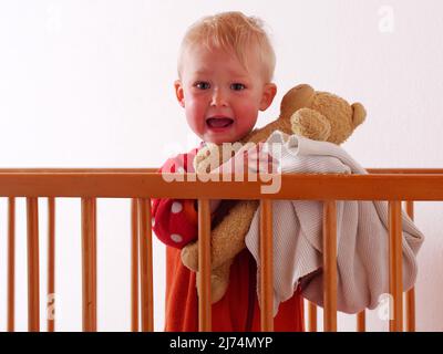 little girl stands crying in bed Stock Photo