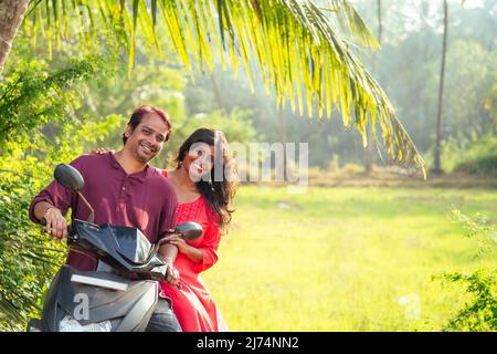 happy indian married couple riding on motorbike adventure in tropical jungle in Goa India copyspace palm trees Stock Photo