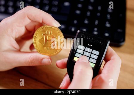 Close up womans hand holding bitcoin and cryptocurrencey hardware cold wallet on keybord background. Secure cryptocurrency storage. Stock Photo