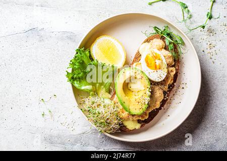 Balanced breakfast toast with pate, avocado, egg and sprouts on a white plate, top view, copy space. Stock Photo