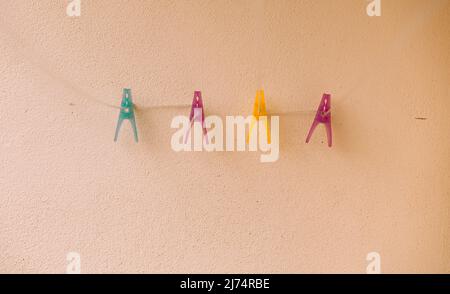 Blue purple yellow clothes pegs hang on the washing line and stand out against a cream wall serving as a background. Stock Photo