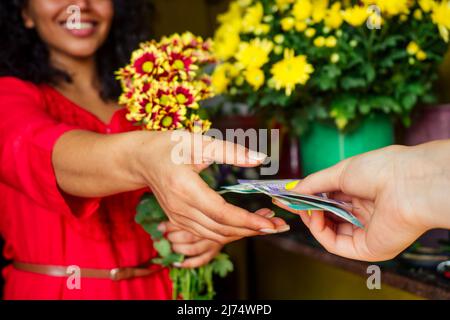 cheerful young woman brunette florist selling flowers in a flower shop taking money from client Stock Photo