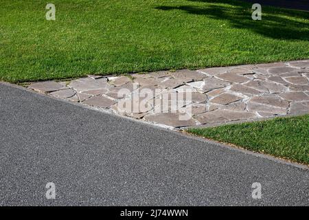asphalt road near garden path made of natural stone paved with rough rock in a park with a green lawn, the decorative path with an abstract pattern. Stock Photo