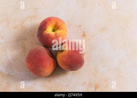 Three peaches on a pink marble backdrop. Stock Photo