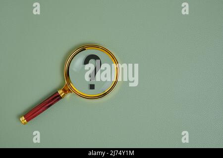 Question mark under magnifying glass, on green background Stock Photo