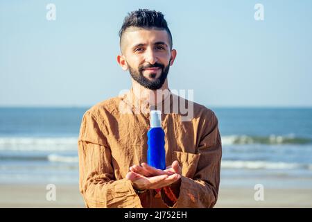 happy young arabian man useing sun cream protect on the beach.Indian male holding a bottle of sunscreen Stock Photo