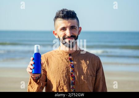 happy young arabian man useing sun cream protect on the beach.Indian male holding a bottle of sunscreen Stock Photo