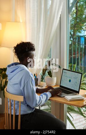 Concentrated young Black woman analyzing data in report on laptop when working from home Stock Photo