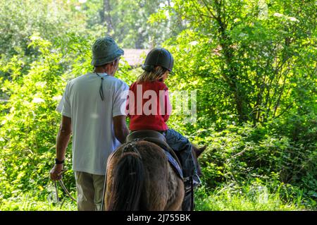 young girl riding poney with father helping on sunny day hobby or activity during holidays . Stock Photo