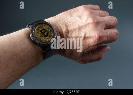 Smart watch with a bitcoin screen on a man's hand, close-up on a gray background. Copy space. Stock Photo