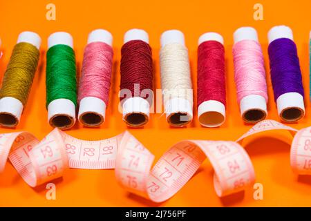 A set of multi-colored threads for sewing and a measuring tape on an orange background, top view. Tailoring and needlework equipment, tailor banner. Stock Photo