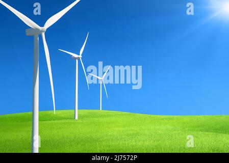 Row of wind generators in a row on top of a hill of green grass against deep blue sky with sunlight Stock Photo