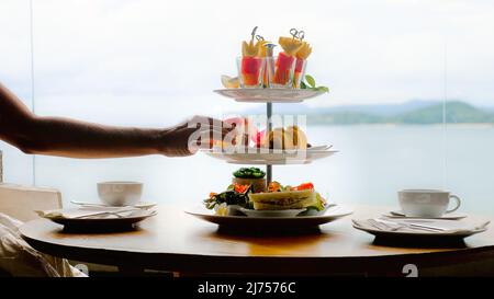 Woman hand takes piece of cake from afternoon tea set for two persons in hotel Stock Photo