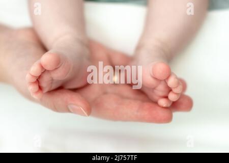 The mother's hands tenderly and lovingly hold the legs of a small child who is several months old from the moment of birth. Stock Photo