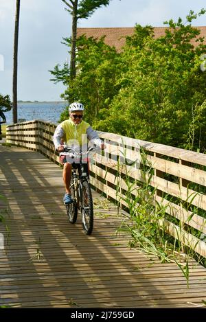Middle age woman pedaling a bicycle on scenic trails and pathways in Gulf State Park, along coastline community of Gulf Shores, Alabama, USA Stock Photo
