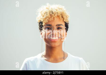 Young brazilian hispanic woman with cool blonde afro curly hair looking through glasses on white background Stock Photo