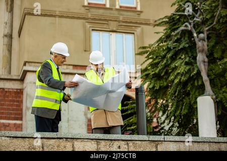 Two construction workers are looking at the plans on the paper while having a discussion Stock Photo