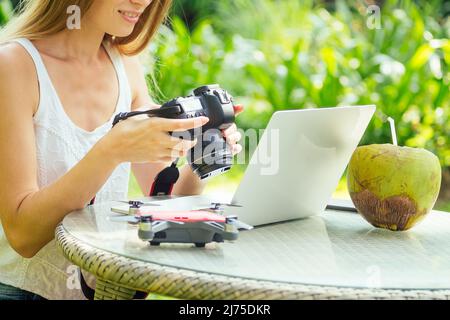 Female photographer inserting or removing a memory card in her professional dslr camera as she sits at a desk with her laptop at paradise beach green Stock Photo