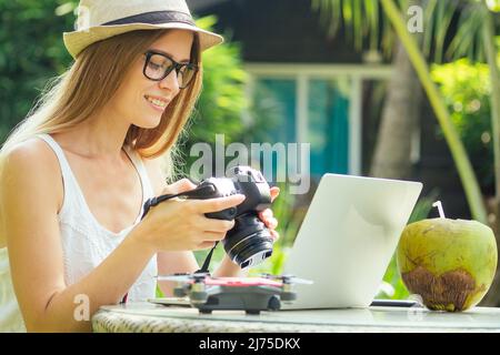 Female photographer inserting or removing a memory card in her professional dslr camera as she sits at a desk with her laptop at paradise beach green Stock Photo