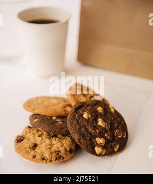 assortment of cookies including chocolate chip, chocolate cookies with white chocolate, and oatmeal with coffee and paper bag in the background Stock Photo
