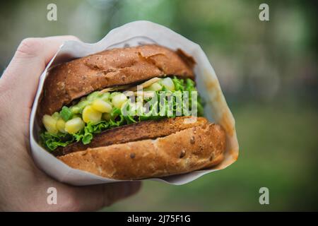 A hand holding a veggie burger with corn, lettuce and guacamole Stock Photo