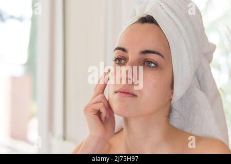 Young Beautiful Girl After Showering with Towel on Head in Bathroom doing Facial Treatment. Skin Care. Performs Morning Procedures before Date. Beauty Stock Photo