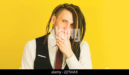 Young happy man looking at camera and scratching chin on yellow background. Positive male smiling, stroking his chin Stock Photo