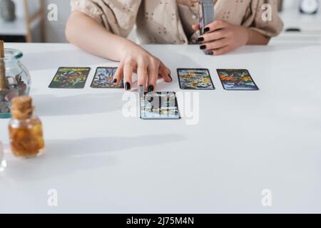 KYIV, UKRAINE - FEBRUARY 23, 2022: Cropped view of fortune teller using tarot cards near witchcraft supplies at home Stock Photo