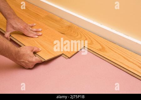Series of shots of engineered hardwood floor being installed by a worker over pink felt paper using hand tools Stock Photo