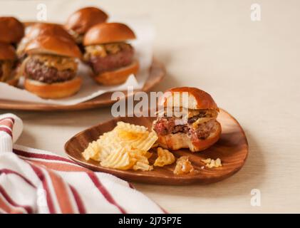 Hamburger Slider with a Bite Taken Out on a Plate with Potato Chips; Platter of Sliders Stock Photo