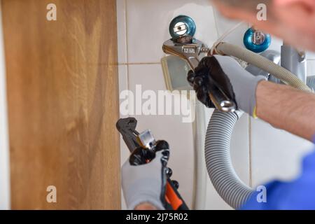 Detail of plumber checking water installation under the sink with wrench and gloves. Horizontal composition. Stock Photo