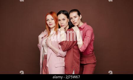 Diverse young multi-ethnic women standing one after another against brown background Stock Photo